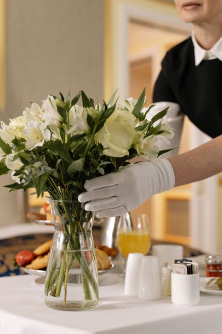 A bouquet of fresh white flowers, including roses and lilies, with lush green leaves, arranged in a clear glass vase. The flowers are vibrant and well-hydrated, with soft petals and sturdy stems. The 